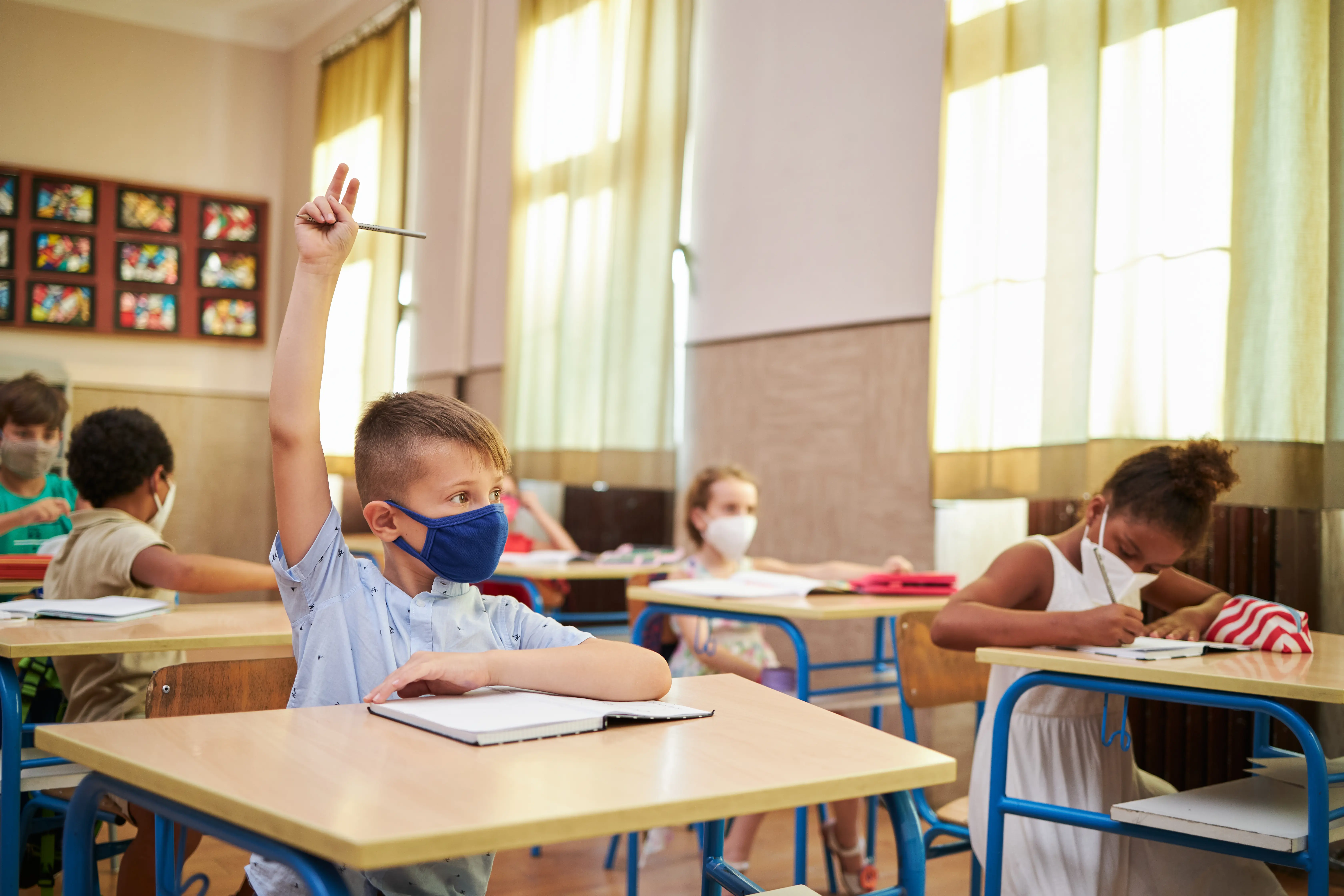 Diligent and curious elementary school students sitting in their classroom and carefully observing the class while wearing protective face mask during COVID-19 pandemic